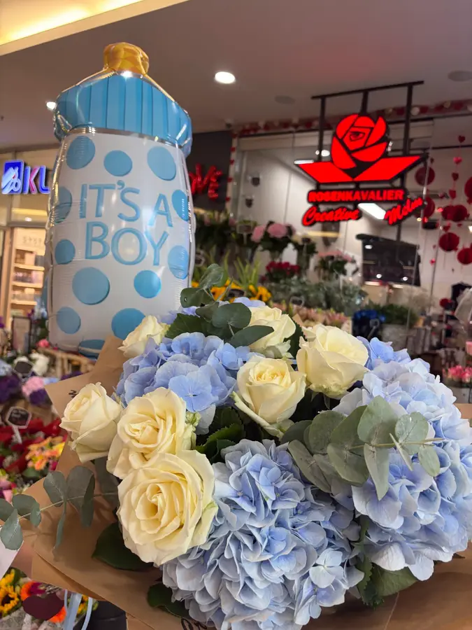 Leuchtschrift „Rosenkavalier Creative Melm“ über dem Laden, davor ein Strauß aus Hortensien und weißen Rosen
