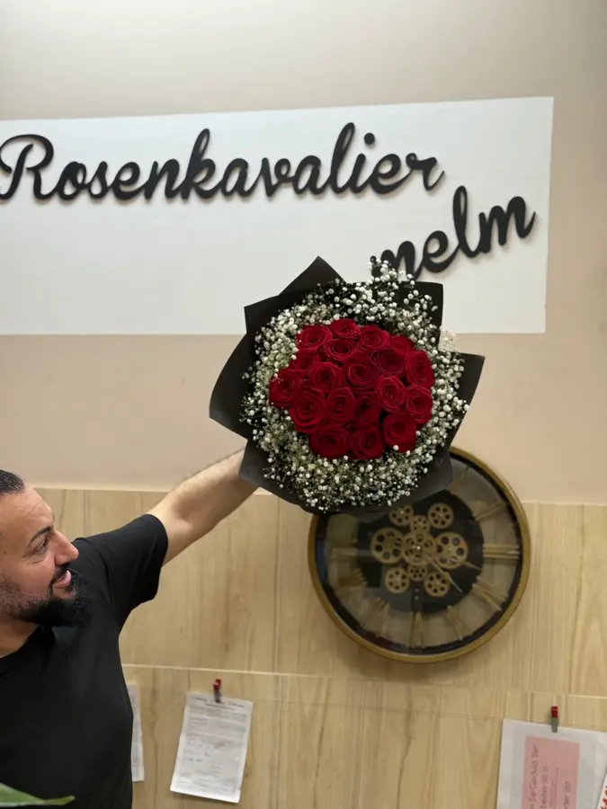 Ein frisch gebundener Strauß roter Rosen mit Schleierkraut wird unter dem Schriftzug „Rosenkavalier Melm“ im Laden hochgehalten
